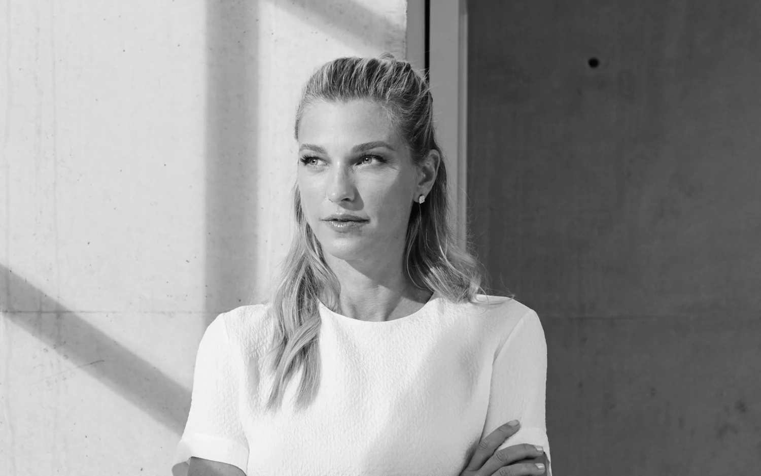 Nicole Junkermann in a white top beside a sunlit concrete wall, a black and white portrait