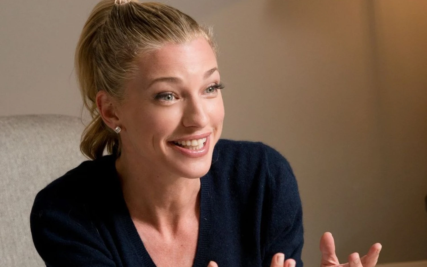 Nicole Junkermann laughing mid conversation in a navy knit, seated in a pale room
